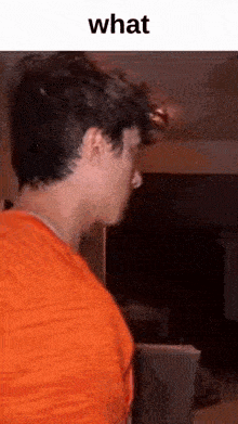 a man in an orange shirt is standing in a living room and looking at something .