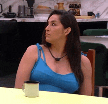a woman in a blue tank top sits at a table with a cup of coffee
