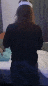 a woman wearing a white headband and a black shirt is standing in front of a bed .