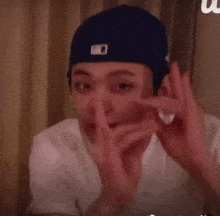 a young man wearing a hat and a white shirt is making a peace sign .