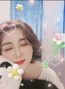 a woman with her eyes closed is holding a stuffed panda bear with flowers and hearts around her head .