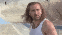 a man with long hair wearing a white tank top