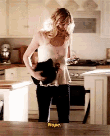 a woman is standing in a kitchen holding a hat and a phone and says nope