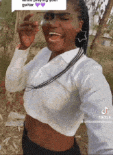 a woman wearing glasses and a white shirt is laughing and holding a guitar