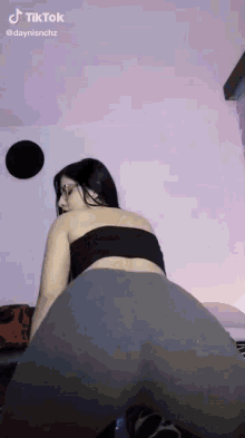 a woman in a black top and gray leggings is dancing on a bed in a room .