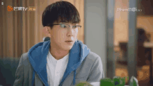a young man wearing glasses is sitting at a table in front of a tv screen