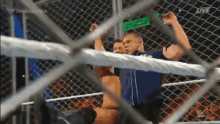 a man in a blue shirt is behind a chain link fence holding a green bottle .
