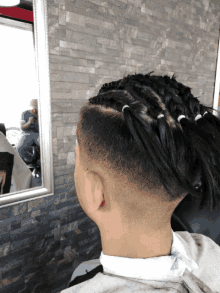 a man with braids and a shaved head looks at his reflection in a mirror