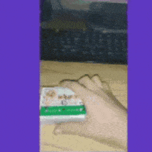 a person is holding a box of cigarettes in their hand in front of a keyboard .