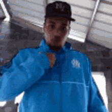 a man wearing a blue jacket and a hat is standing in a room .