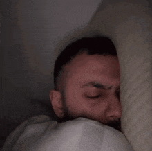 a man peeking out from under a pillow with his eyes closed