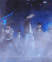 a group of people are dancing on a stage in a dark room with smoke coming out of it .