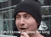 a man wearing a black beanie is talking into a microphone and says i don t know if i know the song