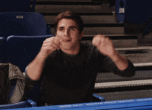 a man in a black shirt is sitting in a boxing ring with his hands in the air