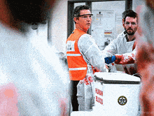 a man in an orange vest stands in front of a box that says human blood