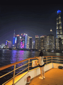a woman stands on the deck of a boat looking at the skyline at night