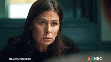 a woman in a black shirt is sitting in a dark room with a nbc logo in the corner
