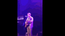a man is playing a guitar on a stage with purple lights .