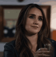 a woman in a black leather jacket is holding a glass