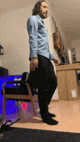 a man in a blue shirt is standing next to a chair in a room
