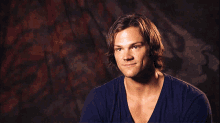 a man with long hair and a blue shirt smiles