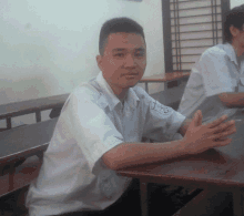 a man sits at a table with his hands folded and a patch on his sleeve that says ' a ' on it