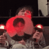 a man is sitting on a couch holding a fan and a red light behind him .