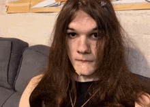 a young man with long hair is sitting on a couch and looking at the camera