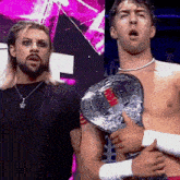 two men are standing next to each other and one is holding a championship belt