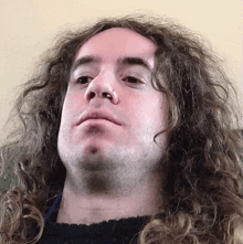 a man with long curly hair has a nose ring on his nose