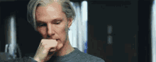 a man with gray hair is biting his nails while wearing a gray sweater .