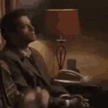 a man in a suit and tie is sitting in a chair with a lamp in the background .