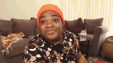 a man wearing an orange beanie is sitting on a couch .