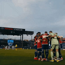 a group of soccer players huddle together in front of a toyota stadium sign