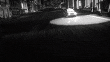 a black and white photo of a police car driving down a city street at night .