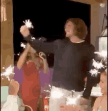 a man is holding sparklers in his hand while dancing in a room with other people .