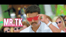 a man wearing sunglasses and a mustache is standing in front of a group of women with the words mr.tk above him