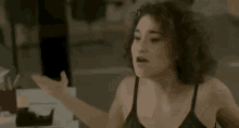 a woman in a black tank top is sitting at a desk with her hands outstretched .