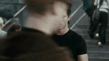a man in a black shirt is sitting on a set of stairs talking to another man .