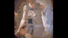 a man wearing a tank top with the letter r on it is standing in a room with other people .