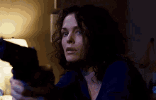 a woman in a blue shirt is holding a gun in her hand in a dark room .