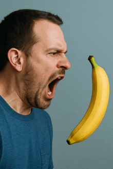 a man in a blue shirt is screaming while holding a banana in his mouth