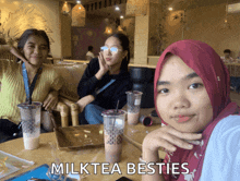 three women are sitting at a table with milk tea cups in front of them