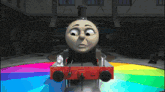 a train with a sad face is on a rainbow colored track