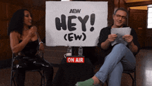 a man and a woman are sitting in front of a sign that says hey