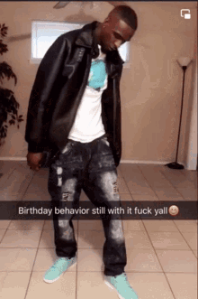 a man wearing a black leather jacket and jeans is standing in a room with a birthday behavior still with it