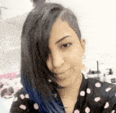 a woman with blue hair and a shaved side is smiling and wearing a polka dot shirt .