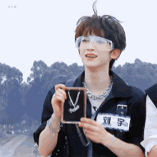 a young man wearing glasses and a necklace is holding a picture frame