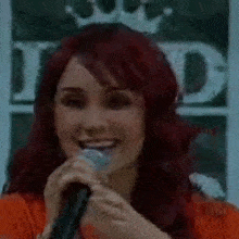 a woman with red hair is smiling while holding a microphone .