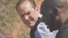 two men are standing next to each other in a field and one of them is looking at the camera .